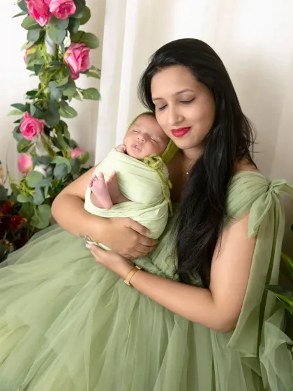 A mother tenderly holds her sleeping newborn, wrapped in a light green swaddle that matches her beautiful dress.