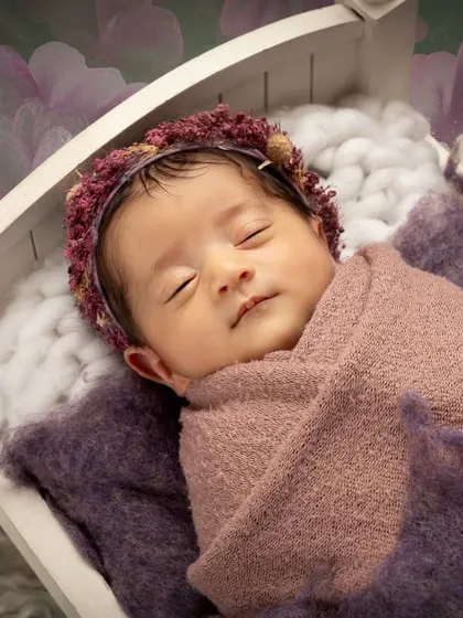 I focus on creating a safe and peaceful environment for your little one. This classic posed newborn portrait captures the serene beauty of a sleeping baby, nestled comfortably in a miniature white cot.