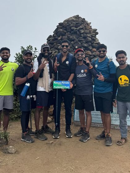 A group of friends celebrating at the Kumara Parvatha peak. The sign they are holding is a fun prop for a memorable photo.