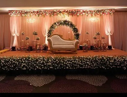 A wide view of a classic floral reception stage. The design includes a central floral arch for the couple's seating and a stage front lined with dense flowers, creating a lush and romantic atmosphere.