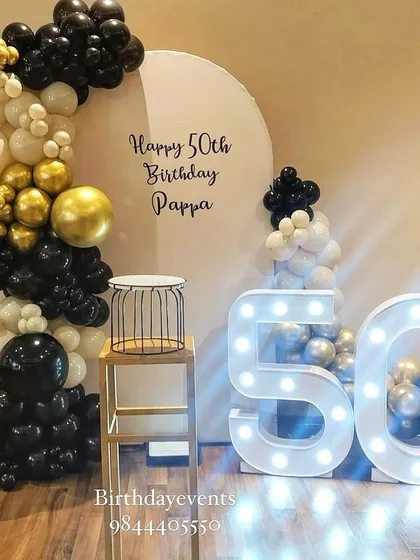 An elegant and sophisticated 50th birthday decoration for a very special celebration. The classic black, white, and gold chrome balloon arch pairs perfectly with the large marquee numbers, creating a timeless and celebratory photo corner.