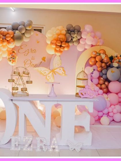 A sophisticated butterfly-themed first birthday. The decor uses a muted color palette of peach, grey, and pink, with a large 'ONE' table and elegant butterfly accents.