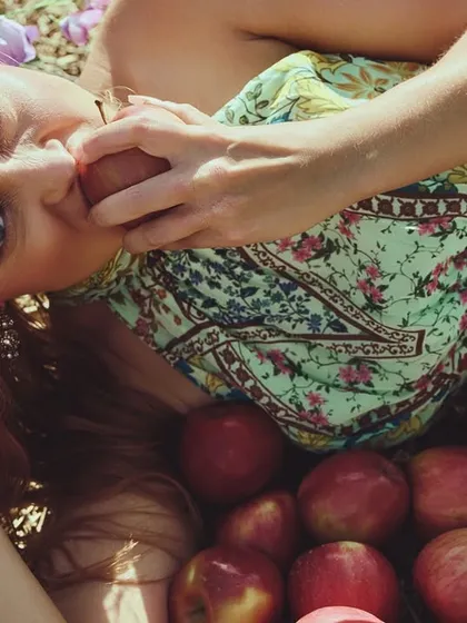 An outdoor fashion shot with a dreamy, ethereal quality. The model is surrounded by apples, creating a scene that feels both natural and staged, like a modern fairytale.
