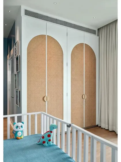 The arched wardrobe doors with cane webbing in the nursery add a touch of warmth and natural texture, balancing the cool blue tones of the room.