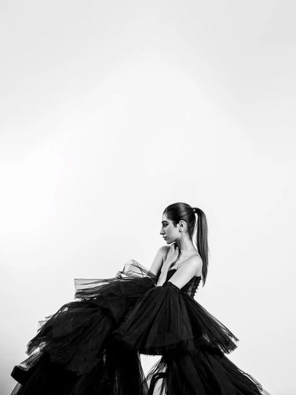 A black and white portrait emphasizing the dramatic volume and texture of a black tulle gown. The mood is elegant and mysterious.