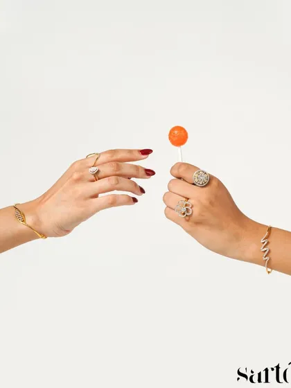 A fun, minimalist shot of two hands sharing a lollipop, both adorned with beautiful rings and bracelets. This image tells a story of friendship and shared moments, making the jewellery feel youthful and modern.