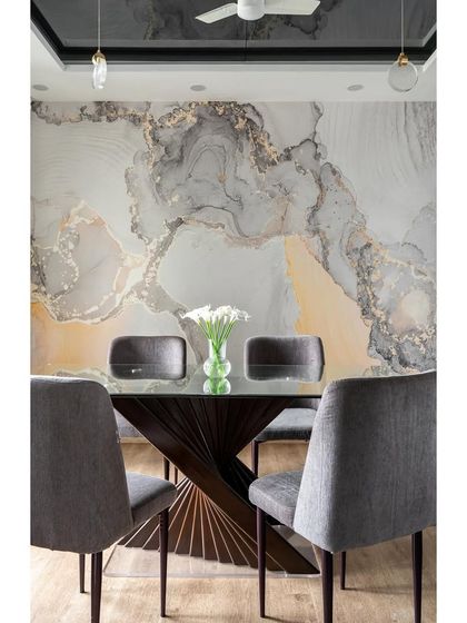In this Mumbai apartment, I used a dramatic, custom wallpaper with a gold and grey marble effect to create a luxurious dining backdrop. The dark wood table with its sculptural base adds to the room's sophisticated feel.