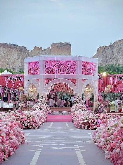 A wide view of the pink mandap, showcasing the aisle lined with thousands of flowers and the elegant structure set against the rugged landscape. It was a beautiful contrast of nature and design.