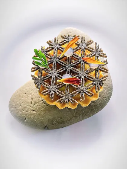 A corn tartlet with a delicate lattice top, served on a river stone. Presentation is key to the overall dining experience.