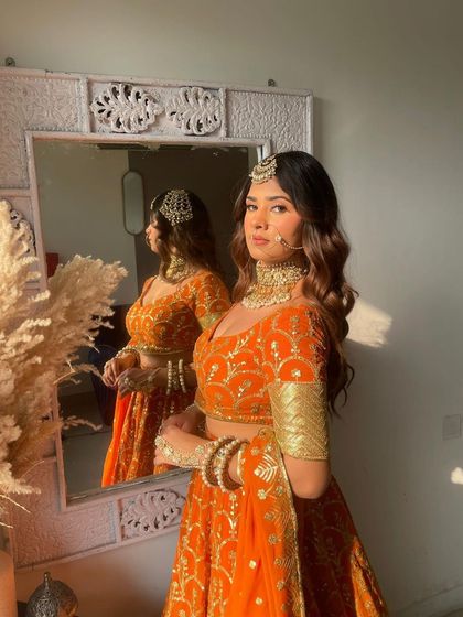 A sunlit shot of a model in a bright orange bandhani print lehenga. The natural light makes the color pop, showing its beauty for a daytime event.