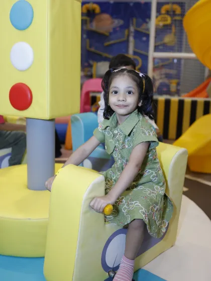A young girl smiles while playing on a soft, traffic-light-themed play structure in the toddler zone.