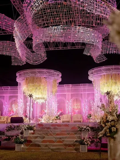 A wider angle of the reception stage, showing how the massive ceiling installation frames the entire area. The soft pink lighting enhances the romantic and ethereal quality of the design.