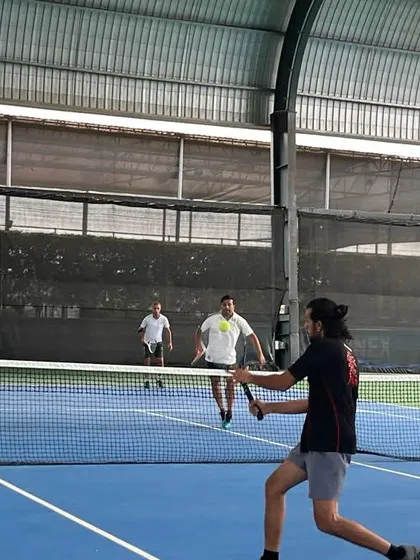 An adult player hits a forehand volley at the net during a competitive doubles match. Our programs help players of all levels sharpen their skills.