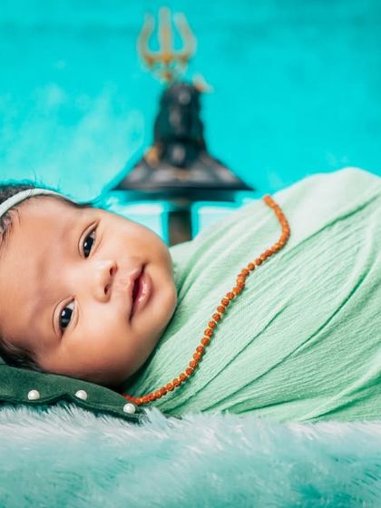 A close-up portrait from the Shivratri session, focusing on the baby's adorable face against the backdrop of the Trishul. The soft lighting and gentle expression make this a precious memory.