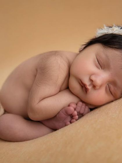 The 'taco' pose on a warm, neutral backdrop. This pose is always done gently and safely to ensure the baby is comfortable.