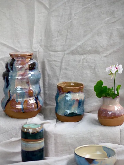 A collection of student work featuring wavy, organic forms and beautiful, flowing blue and brown glazes. These pieces have a lovely, earthy feel.