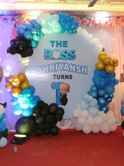 A large Boss Baby themed stage for a first birthday party, featuring multiple character cutouts and a circular backdrop.