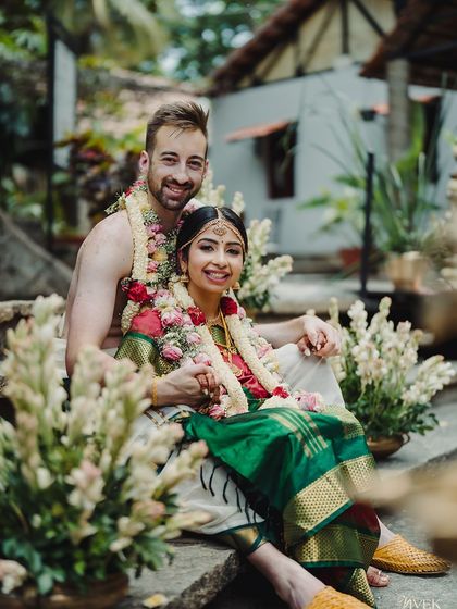 A cross-cultural couple shares a smile, seated on the stone steps of the kalyani. The floral arrangements add to the celebratory and romantic feel.