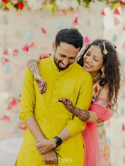 The bride playfully shows the groom something on her mehendi-adorned hand, sharing a laugh. This candid photo captures the sweet and easy chemistry between the couple during their pre-wedding festivities.