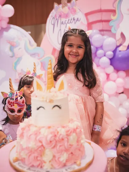 The birthday girl, Maseera, smiling brightly next to her adorable unicorn-themed cake.
