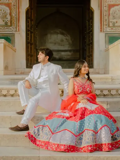 Seated on the steps of a historic entrance, this pose is both regal and relaxed. The bride's colorful lehenga spreads out beautifully, creating a stunning visual for their pre-wedding collection.