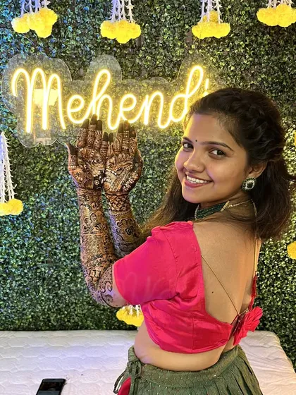 A modern and chic Mehendi setup. We use a lush green artificial wall as the base, adding a custom neon sign for the event and delicate floral hangings to complete the look.