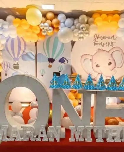 A first birthday party with an elephant and hot air balloon theme, featuring large 'ONE' letters and a custom backdrop.