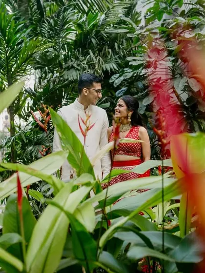 A creative portrait of the couple in a lush garden, viewed through vibrant foreground flowers. This framing technique adds depth and a touch of mystery to the romantic scene.