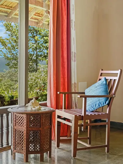 A simple wooden chair and an intricately carved side table sit by a window, offering a view of the hills. This quiet corner is an invitation to sit, relax, and soak in the scenery.