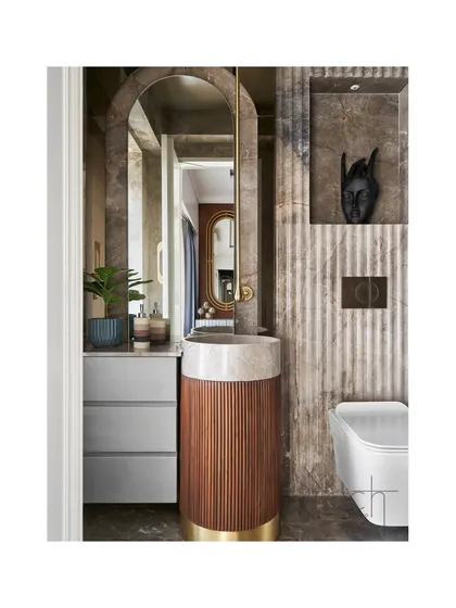 The powder room features a gracefully arched backlit mirror and a bespoke pedestal basin crafted from wood, marble, and brass. The design transforms a functional space into a haven of aesthetic elegance.