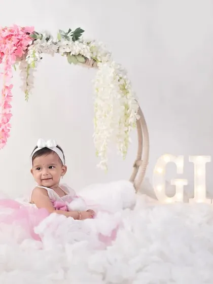 A dreamy first birthday portrait of baby Gia, sitting on a cloud-like setup with her name in marquee lights.