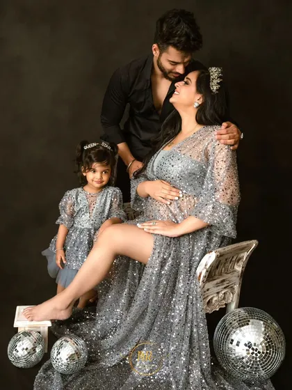 A complete family portrait filled with love. The family of three, soon to be four, poses together in a classic studio setup with glamorous matching outfits.