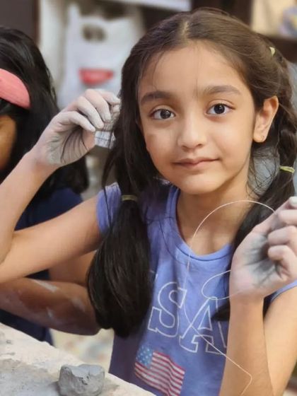 A young girl carefully cuts a piece of clay with a wire tool. We teach students of all ages how to use pottery tools safely and effectively to achieve their artistic vision.