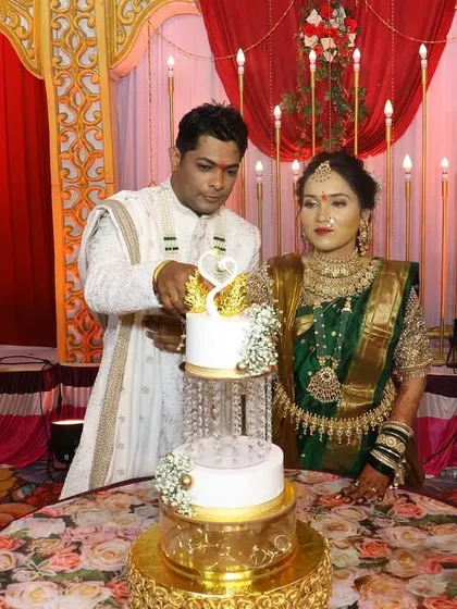 A beautiful moment from an Aagri-Koli engagement ceremony. The couple cuts our two-tier cake with a swan topper and crystal separators, surrounded by traditional decor.