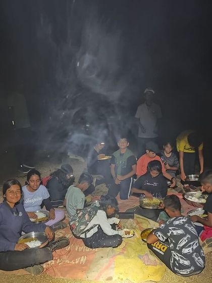 The camp circle enjoys a meal together around the smoky campfire, sharing stories and food.