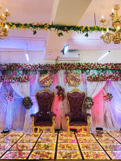 An elegant stage decoration perfect for an engagement or wedding reception at our Badlapur banquet hall. The setup features grand 'king and queen' chairs, a beautiful floral backdrop with sheer curtains and mood lighting, and an LED floor to create a royal ambiance.