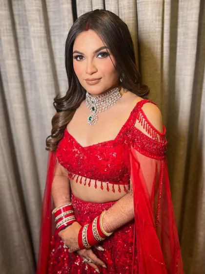 A classic bridal look in red, with hair styled in soft, voluminous waves that cascade over the shoulders, complementing the traditional chooda and diamond necklace.