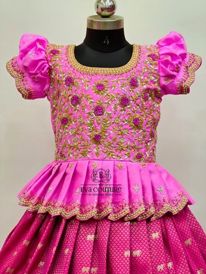 A close-up of a pink blouse covered in dense floral maggam work. The gold thread and beadwork create a luxurious texture.