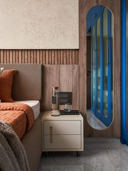 A view of the guest room showing the contrast between the warm wood textures, the cool blue of the wardrobe, and the neutral beige tones of the bed and walls.