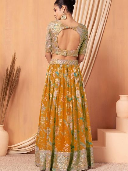 A pop of color for your celebration. This orange organza lehenga with a sequined blouse and floral skirt is designed for a fun and festive event like a Haldi or Sangeet.