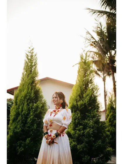 A portrait of the bride on her Haldi day, standing tall and smiling. The natural setting and her bright attire create a fresh and joyful image.