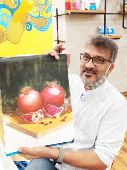 A student holds his realistic still-life painting of pomegranates, showcasing his skill in capturing light, shadow, and texture.
