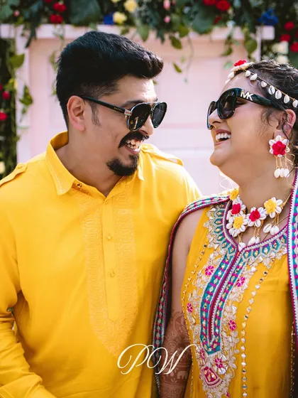 A happy couple, laughing and enjoying their tropical-themed Haldi. Their coordinated yellow outfits and floral jewelry complete the look.