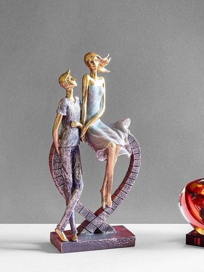 This sculpture portrays a couple in a modern, elongated style, seated on a heart-shaped base. It's a contemporary and artistic representation of love and connection.