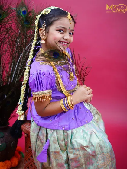 A beautiful portrait of a young girl in traditional South Indian attire, with a "moggina jade" (floral braid) and peacock feathers. Her smile is absolutely radiant.