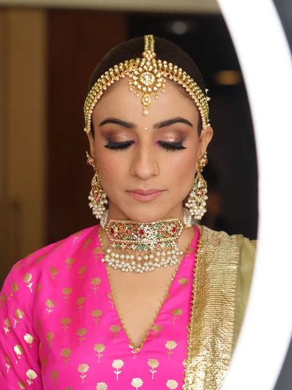 A serene moment as the bride gets her makeup done. The ring light creates a beautiful, soft glow, highlighting her stunning jewelry and the artist's work.