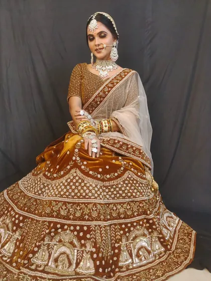A bride wearing a rich brown velvet lehenga with doli embroidery on the border. This is a unique and royal color choice for a winter bride.