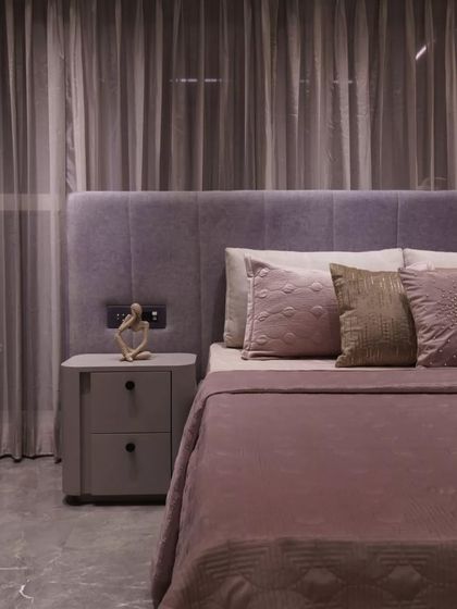 This bedroom space is designed with a soft mauve palette and a tactile mix of velvet and textured fabrics for a soothing ambiance. Sheer drapery adds an ethereal glow, while the sleek marble flooring and curated decor create a balance of warmth and modern sophistication.