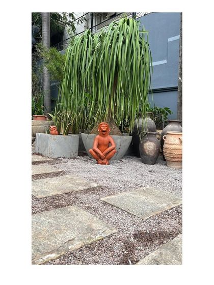 A quirky terracotta monkey sculpture sits among various pots and planters at Peacock Life. The landscape design incorporates playful and artistic elements to match the brand's aesthetic.