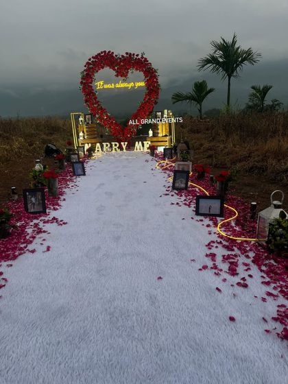 A wide view of our hillside proposal decoration, showing the full path leading to the 'Marry Me' marquee letters and the heart-shaped floral arch. The natural landscape in the background adds to the epic scale of the moment.